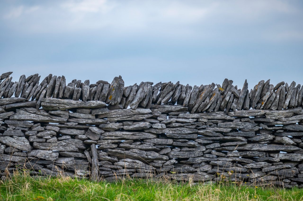 Ancient Stone Wall on Inis Oírr clouded sky above and green grass at the bottom of the picture 