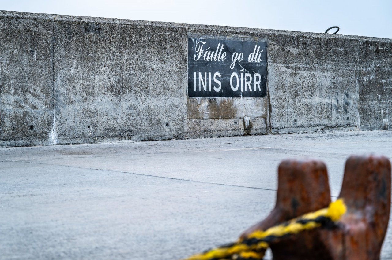 Concrete Pier at Inis Oírr - Black banner in the middle of the picture advertising accommodation on the island in Gaelic. Steel oxidised anchor point on the foreground 